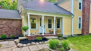 A two-story house with a covered porch, brick foundation, and a landscaped front yard with a stone pathway and a circular planter.