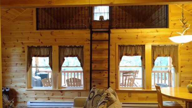 A cozy cabin interior with a wooden interior, a sofa, a dining table, and windows with curtains. - Located in the Finger Lakes a cabin in the country w/ trails & fishing 
 (Cohocton)