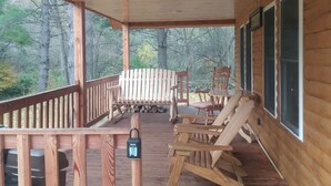 A wooden deck with a table and chairs, a rocking chair, and a bench. - Located in the Finger Lakes a cabin in the country w/ trails & fishing 
 (Cohocton)