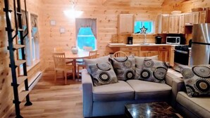 A cozy cabin interior with a wooden dining area, a sofa with patterned cushions, and a kitchen with wooden cabinets and appliances. - Located in the Finger Lakes a cabin in the country w/ trails & fishing 
 (Cohocton)