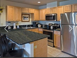 Enjoy cooking in this well-equipped kitchen with a microwave, oven, and refrigerator, featuring a granite countertop and sink.