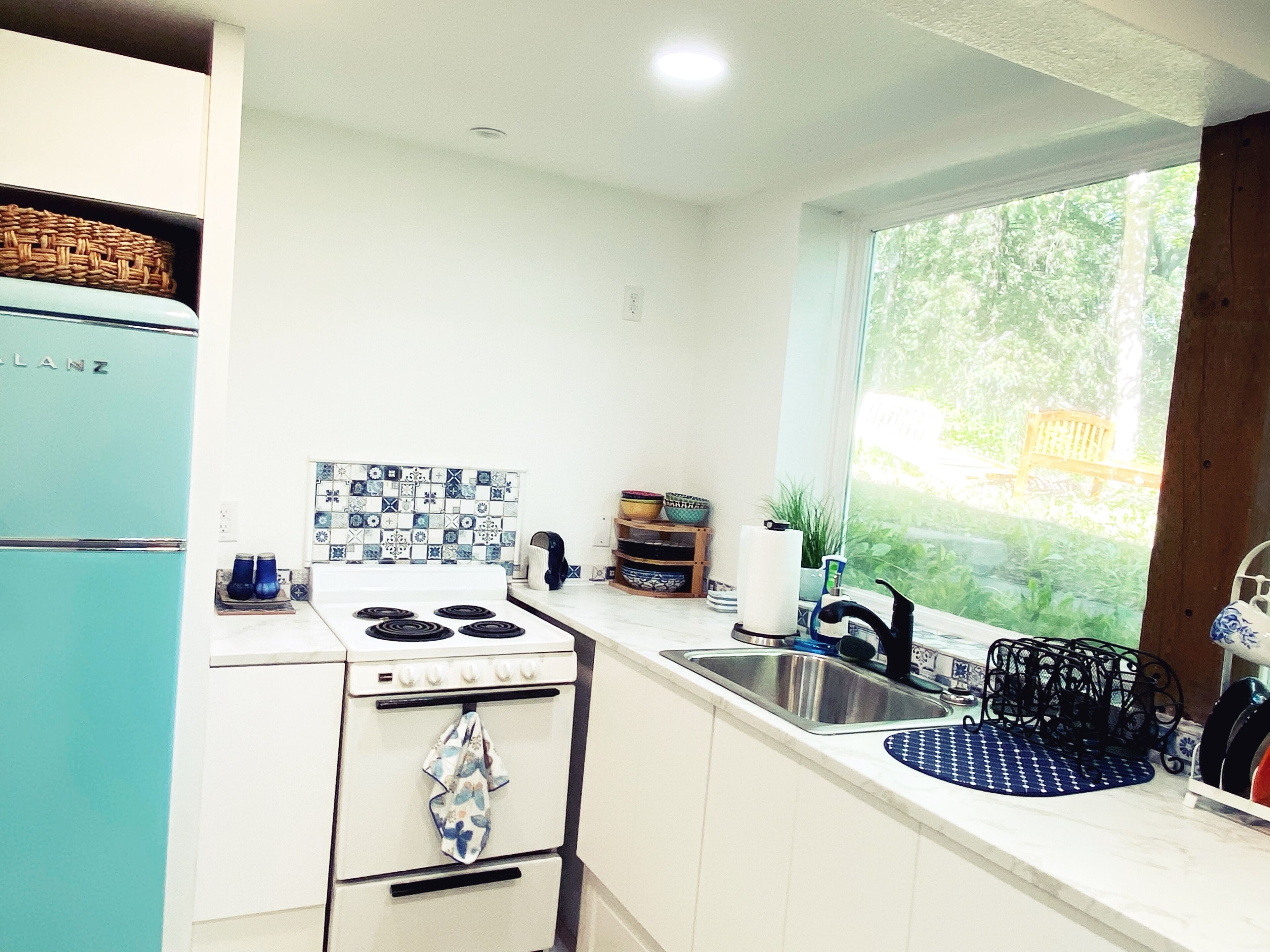 A kitchen with a white stove, a sink, and a window with a view of greenery.