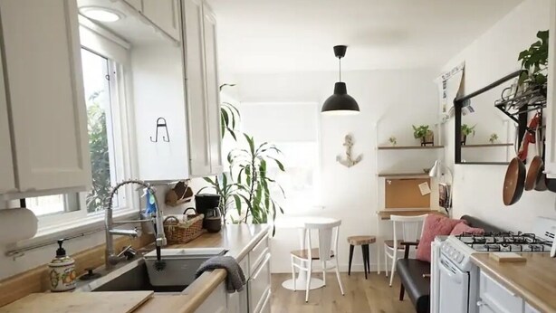 Une cuisine avec des meubles blancs, un plan de travail en bois, un évier, une cuisinière et un coin repas avec des chaises blanches.