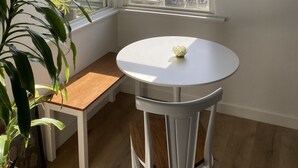 Une pièce d’angle avec une table blanche, un banc, une lampe suspendue et une vue sur les voitures garées à l’extérieur.