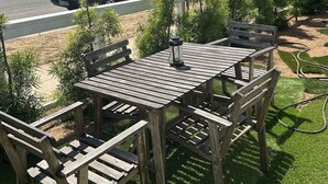 Une terrasse extérieure en bois, avec une table et des chaises, entourée de petits arbres et d’une pelouse.
