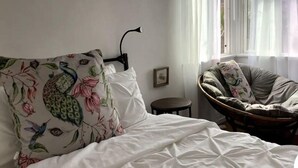 Une chambre à coucher comprenant un lit, une chaise, une table de chevet et une fenêtre avec des rideaux légers.