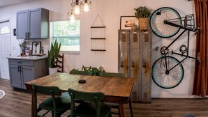 Un coin repas avec une table et des chaises en bois, une cuisine avec des meubles gris et un vélo accroché au mur.