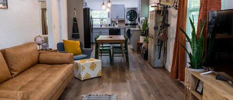 A modern living room with a sofa, a coffee table, and a TV. There is a kitchen area with a dining table and chairs.