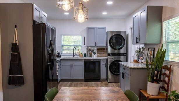 Une cuisine moderne avec des meubles de couleur grise, une table à manger en bois et un lave-linge encastré.