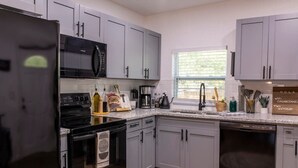 Une cuisine moderne avec des meubles gris, un réfrigérateur noir, une cuisinière et un lave-vaisselle.