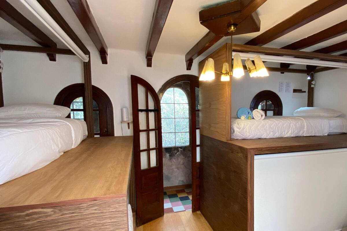 A room with two beds, wooden beams, a small window, and a white radiator.