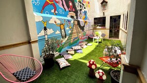 A courtyard with artificial grass, colorful murals, potted plants, and outdoor seating. - Hostal Fungi Casa Rosa (Mexico City)
