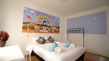 A bedroom with a bed, pillows, a bedside table, a chair, a wall mural, and a starry night wall decal.