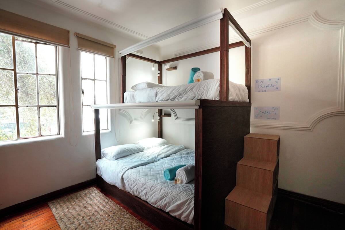 A bunk bed room with a window, a wooden staircase, and name tags on the wall.
