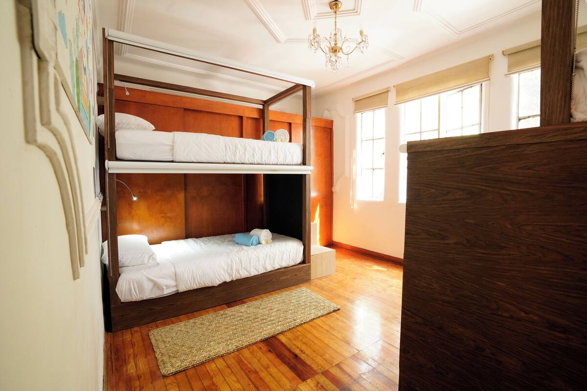A room with a bunk bed, wooden flooring, a chandelier, and a window with a view.