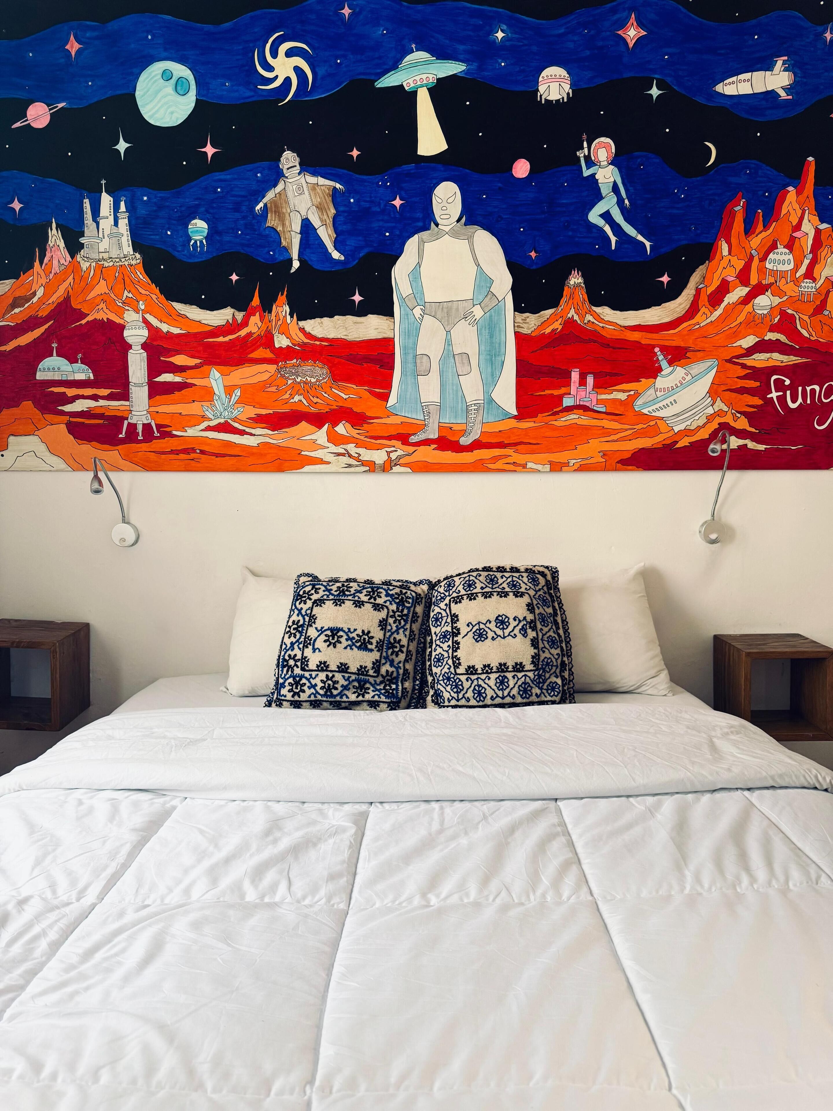 Un dormitorio con cama, ropa de cama blanca y un mural en la pared que representa el espacio y elementos futuristas.