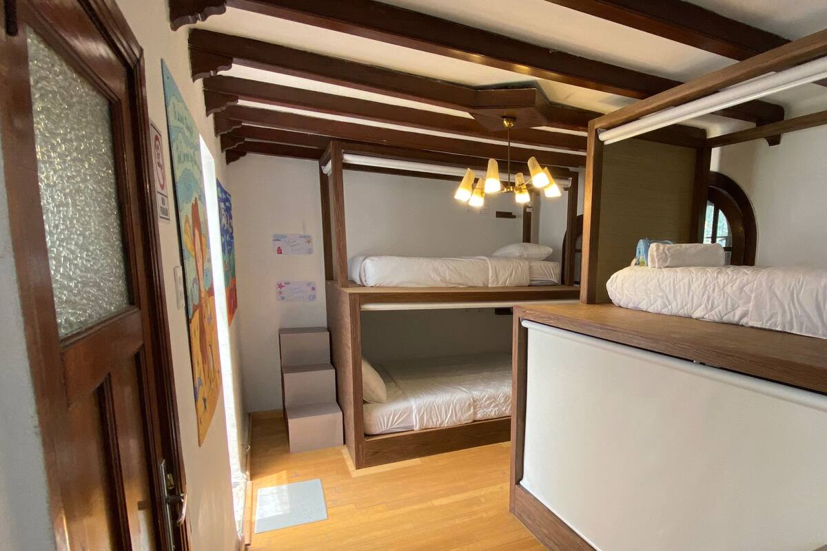 A bunk bed room with wooden beams, a ceiling light fixture, and a window with a view.