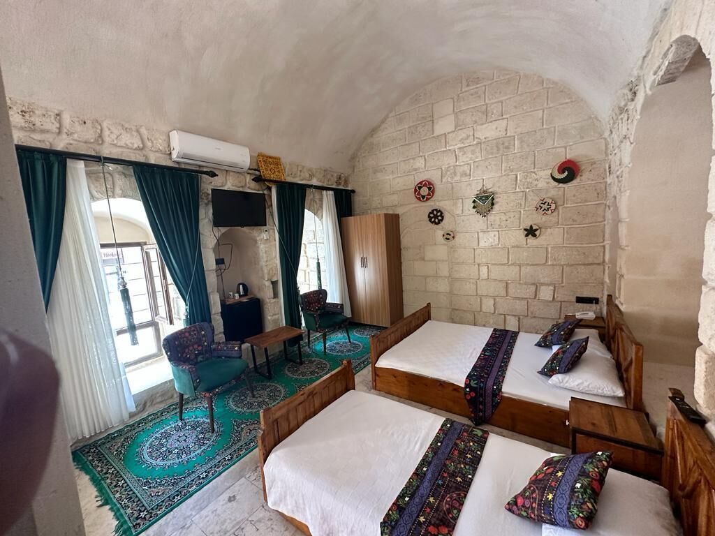 Quarto com três camas de madeira, uma TV, uma cadeira e uma mesa pequena.