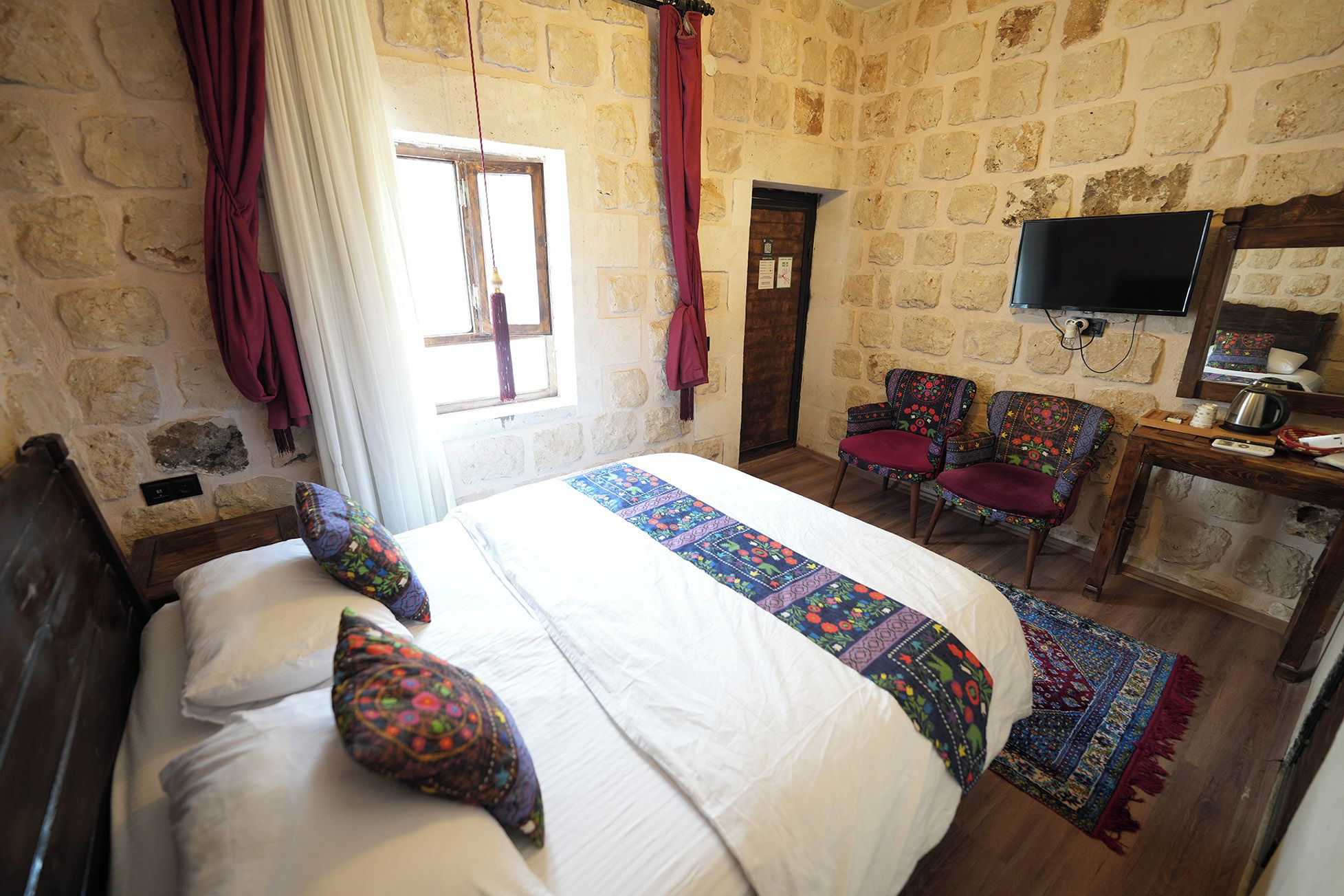 A room with a bed, a chair, a television, and a stone wall.