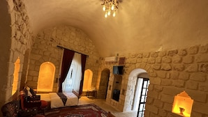 A stone-walled bedroom with a large bed, a red carpet, and a small table with a lamp. - Şikeft Butik Otel (Midyat)