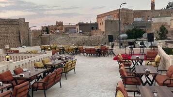 An outdoor seating area with tables and chairs, stone walls, and a view of historic buildings in the background.