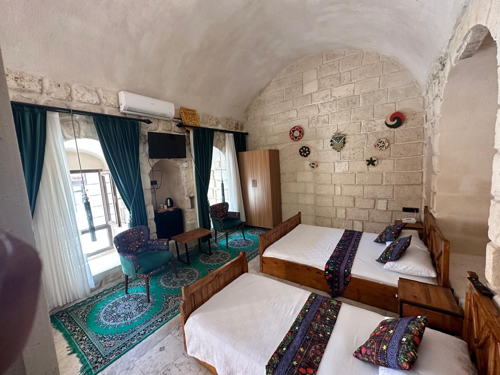 A room with two wooden beds, a small table, a chair, and a TV mounted on the wall.