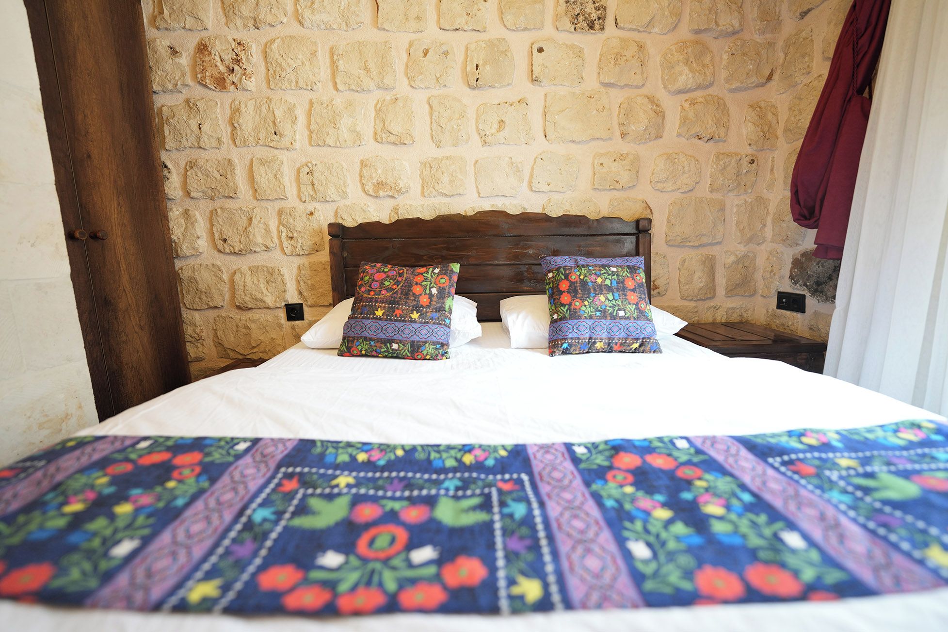 A bed with a patterned bedspread and two decorative pillows, set against a stone wall with a wooden headboard.