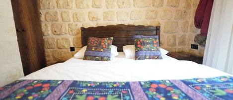 A bed with a patterned bedspread and two decorative pillows, set against a stone wall with a wooden headboard.