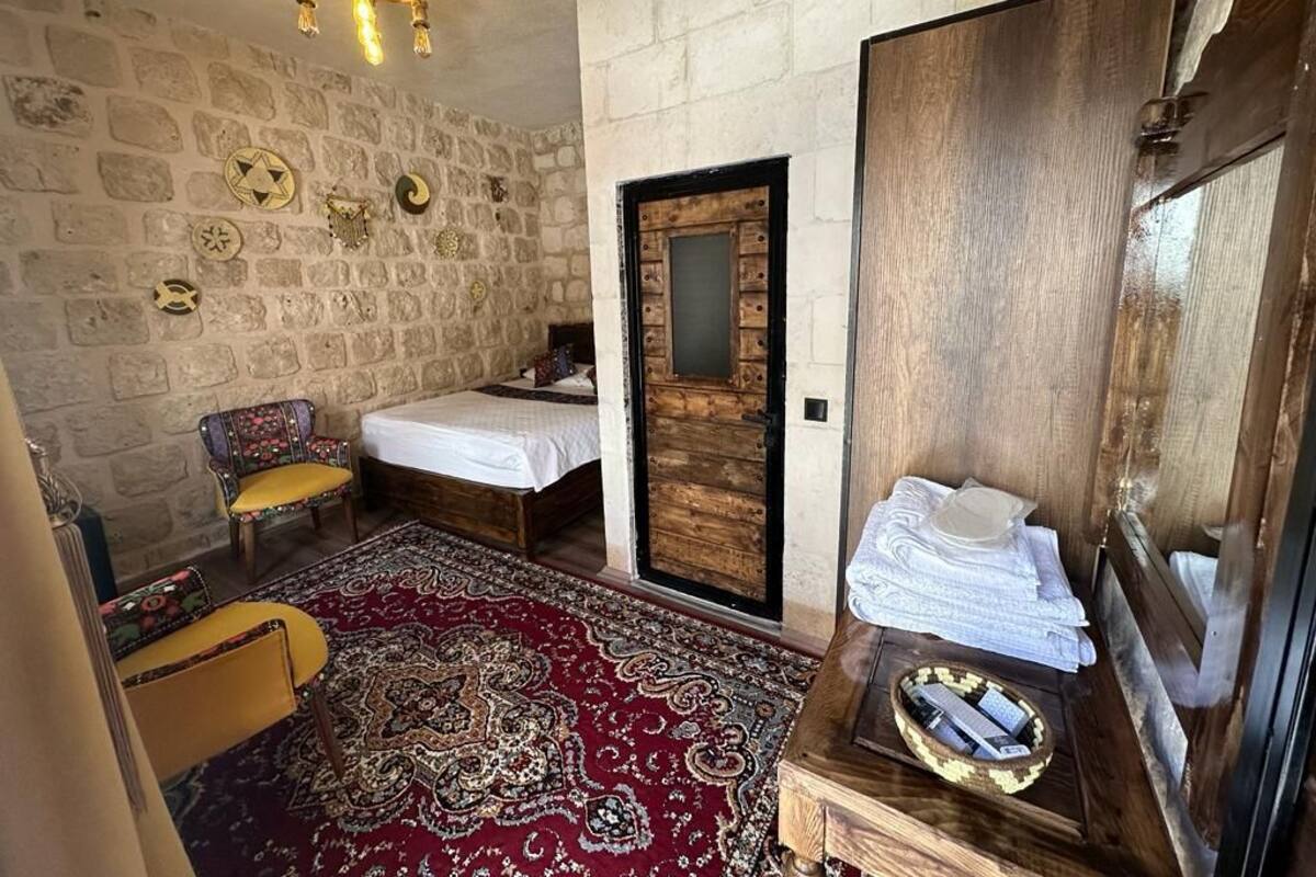 A room with a stone wall, a wooden door, a bed, a chair, and a small table with towels.
