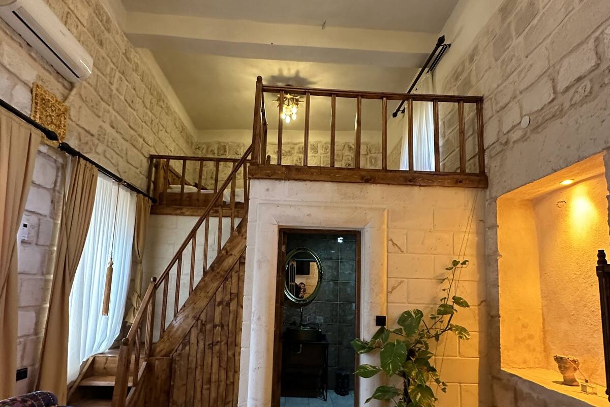 A spacious living area with a high ceiling, a wooden staircase, and a large rug.