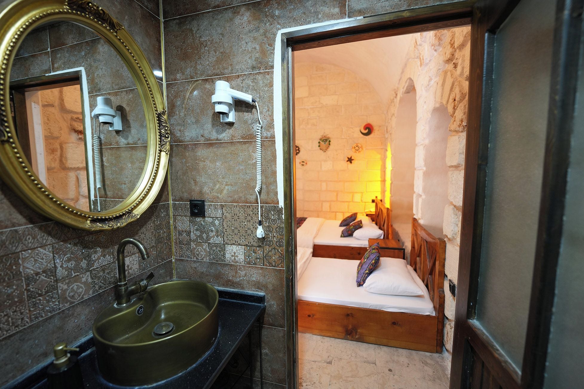 A bathroom with a sink, mirror, and a bed with a wooden headboard.