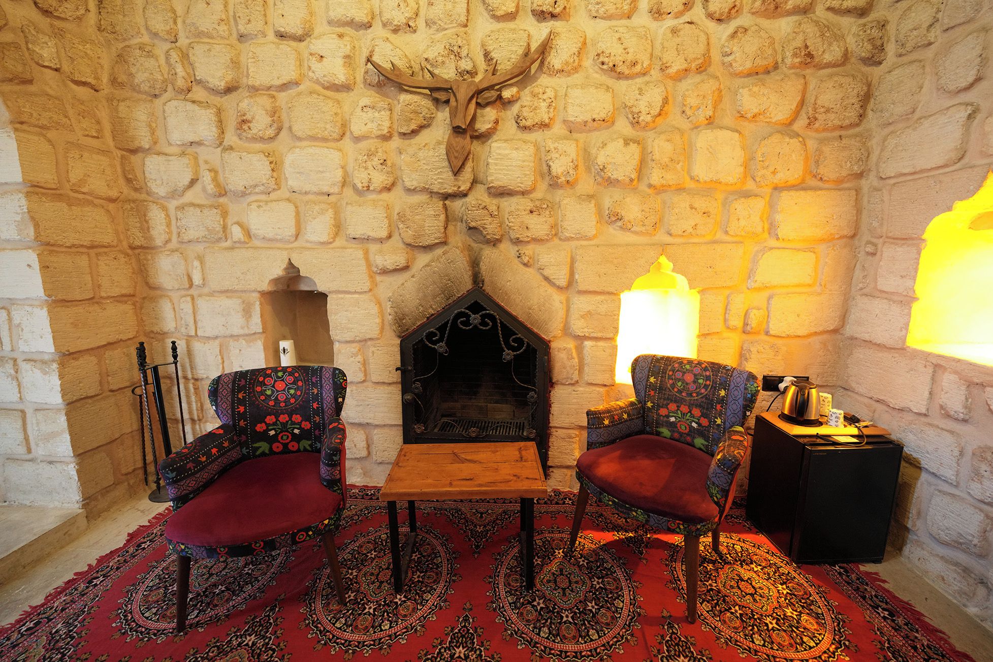 A cozy room with a stone fireplace, two patterned chairs, a small table, and a decorative wall piece.