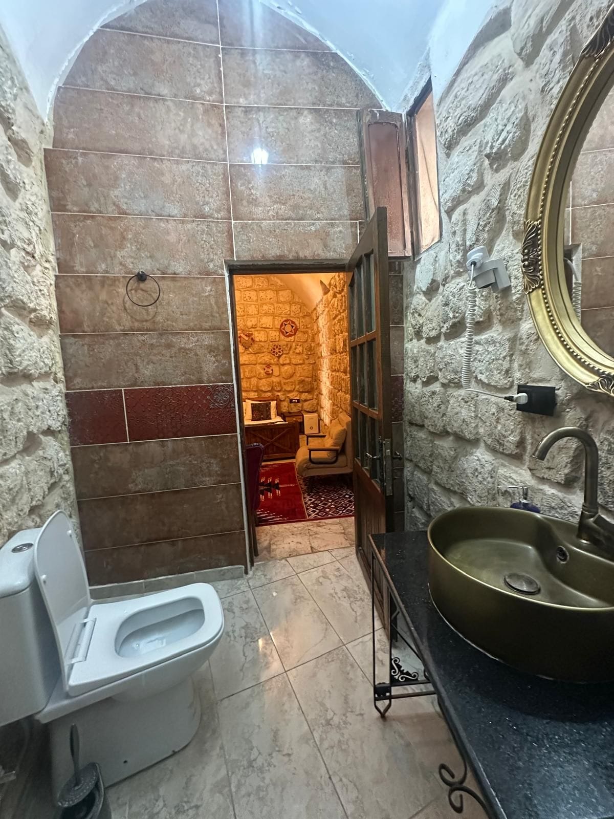 A bathroom with a stone wall, a toilet, a sink, and a mirror.