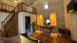 A spacious living area with a wooden staircase, a small window, a television, and a desk with a plant. - Şikeft Butik Otel (Midyat)