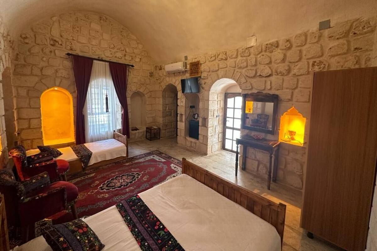 A room with a stone wall, a bed, two chairs, a small table, and a lamp.