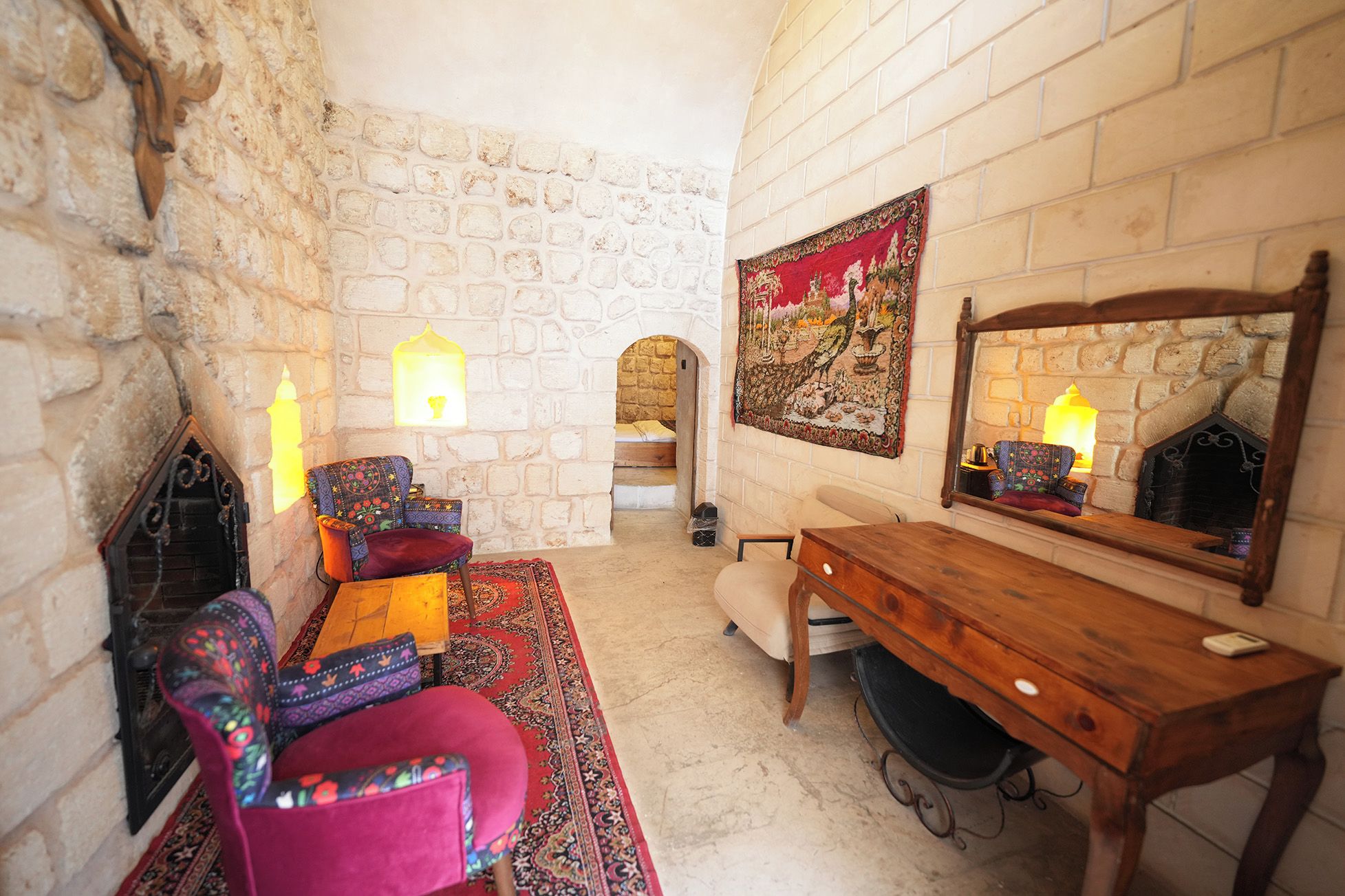 Una habitación con pared de piedra, un escritorio de madera, una silla, un sofá, un tapete estampado y un tapiz.