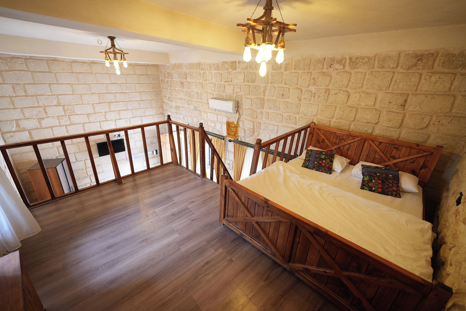A bedroom with a wooden bed, a balcony with a railing, and a stone wall.