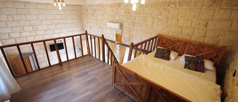 A bedroom with a wooden bed, a balcony with a railing, and a stone wall.