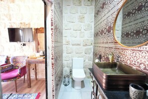 A bathroom with a white toilet, a sink with a brass faucet, and a mirror on the wall. - Şikeft Butik Otel (Midyat)