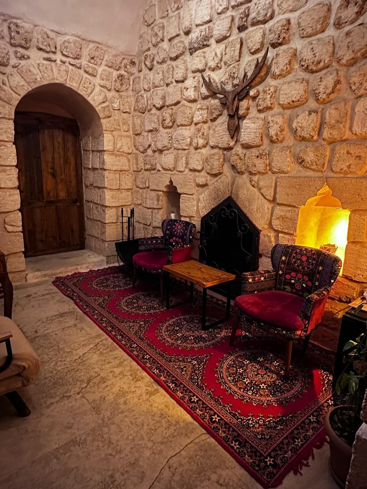 A stone-walled room with a wooden door, a patterned rug, and two upholstered chairs.