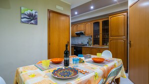 A dining area with a table set for four, featuring orange chairs, a patterned tablecloth, and a bottle of wine. - Angel's Holiday Apartment - Panoramic Relax (San Mauro Castelverde)