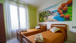 A hotel room with two beds, a painting of cacti and a beach, and a window with curtains. - Angel's Holiday Apartment - Panoramic Relax (San Mauro Castelverde)