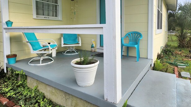 Eine Veranda mit zwei blauen Stühlen, einem weißen Tisch und Topfpflanzen.
