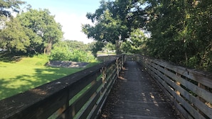 Eine Holzbrücke in einem Park mit grünen Flächen und Bäumen an beiden Seiten.