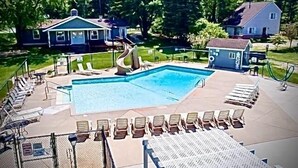 A swimming pool with lounge chairs and a small building, surrounded by trees and houses.