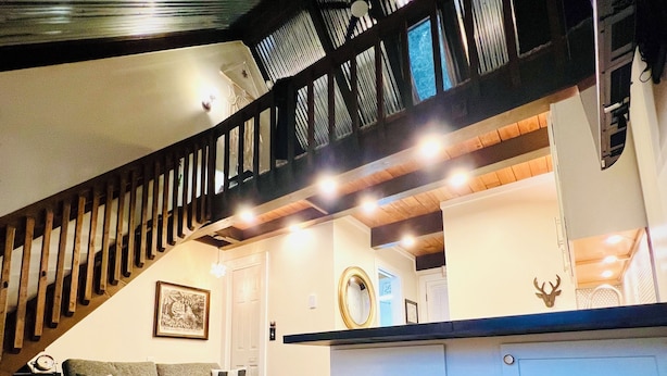 A modern living room with a wooden staircase, a sofa, a coffee table, and a kitchen area with stools. - Charming Loft Cabin - Best Location Davis, Thomas, Canaan Valley. Cold AC (Davis)