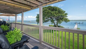 A covered deck with outdoor furniture, a view of a lake, and a dock in the background. - Spectacular ocean getaway, vacation done right! (Beaufort)