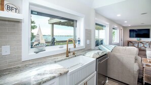 A modern kitchen with a large window overlooking a waterfront, a built-in sink, and a dining area with a view. - Spectacular ocean getaway, vacation done right! (Beaufort)