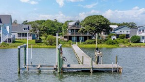 A waterfront property with a dock extending into calm water, surrounded by residential houses and lush greenery. - Spectacular ocean getaway, vacation done right! (Beaufort)