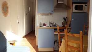 A compact kitchen with a microwave, sink, and wooden cabinets. There is a dining table with chairs and a small table with a chair. - 5mn from the sea studio T1 Banyuls sur mer (Banyuls-sur-Mer)